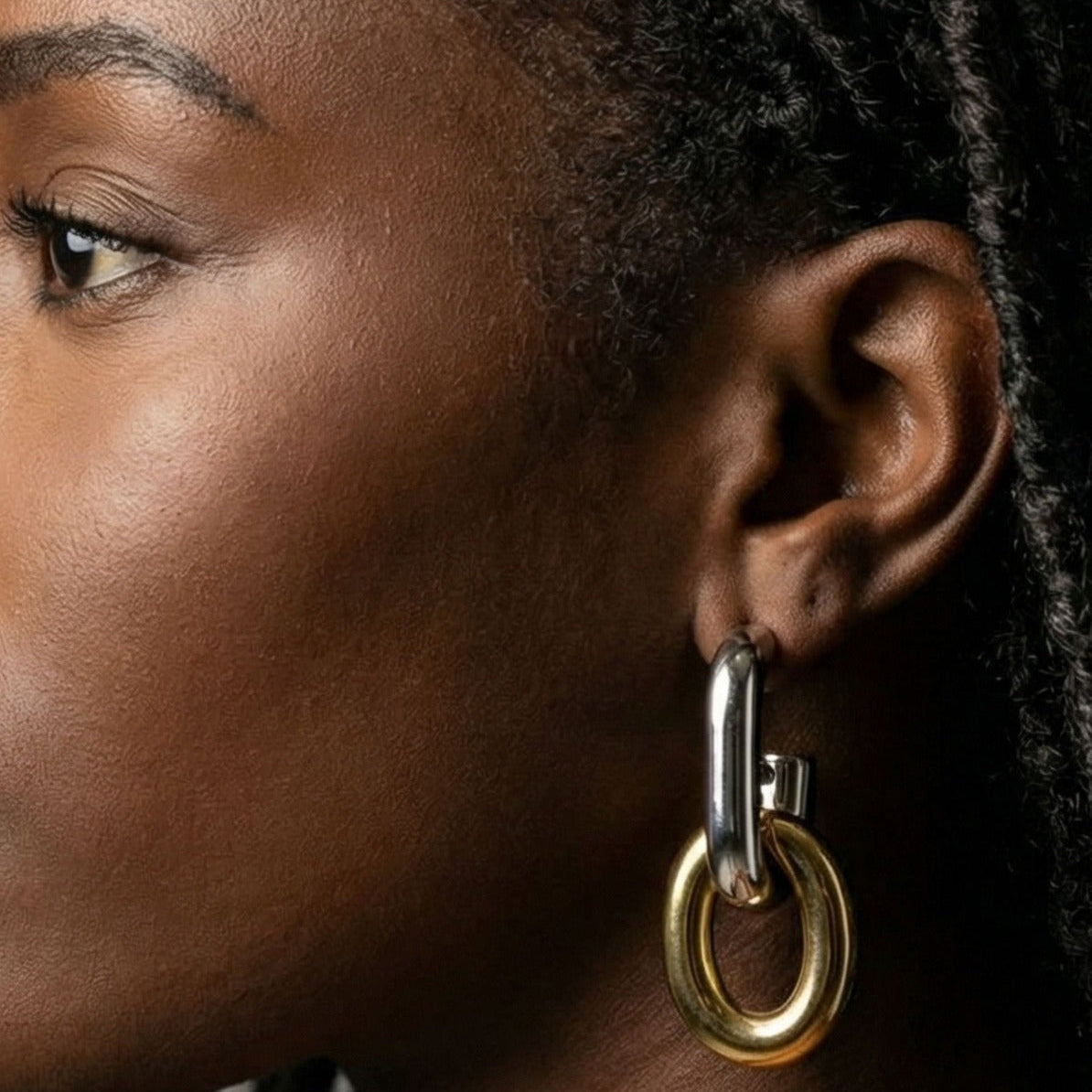 Close-up of a person wearing a gold hoop earring with a dark background