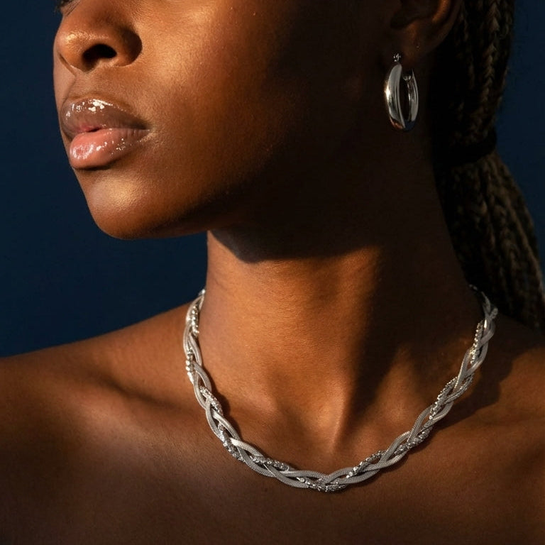 Woman with braided hair wearing a silver necklace and earring against a dark background