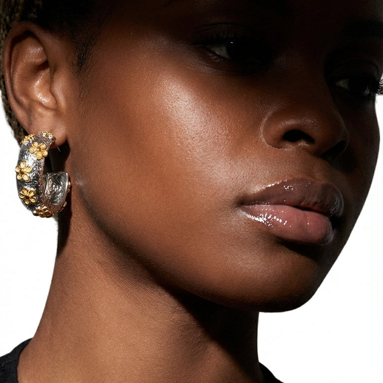 Close-up of a woman wearing gold hoop earrings against a black background