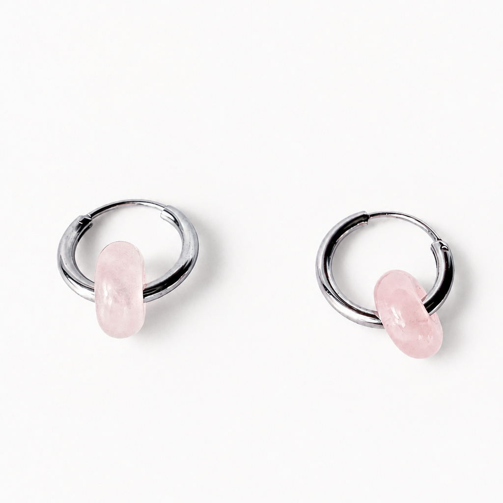 A pair of silver huggie hoop earrings with a small, polished pink stone dangling from each hoop, set against a clean white background.