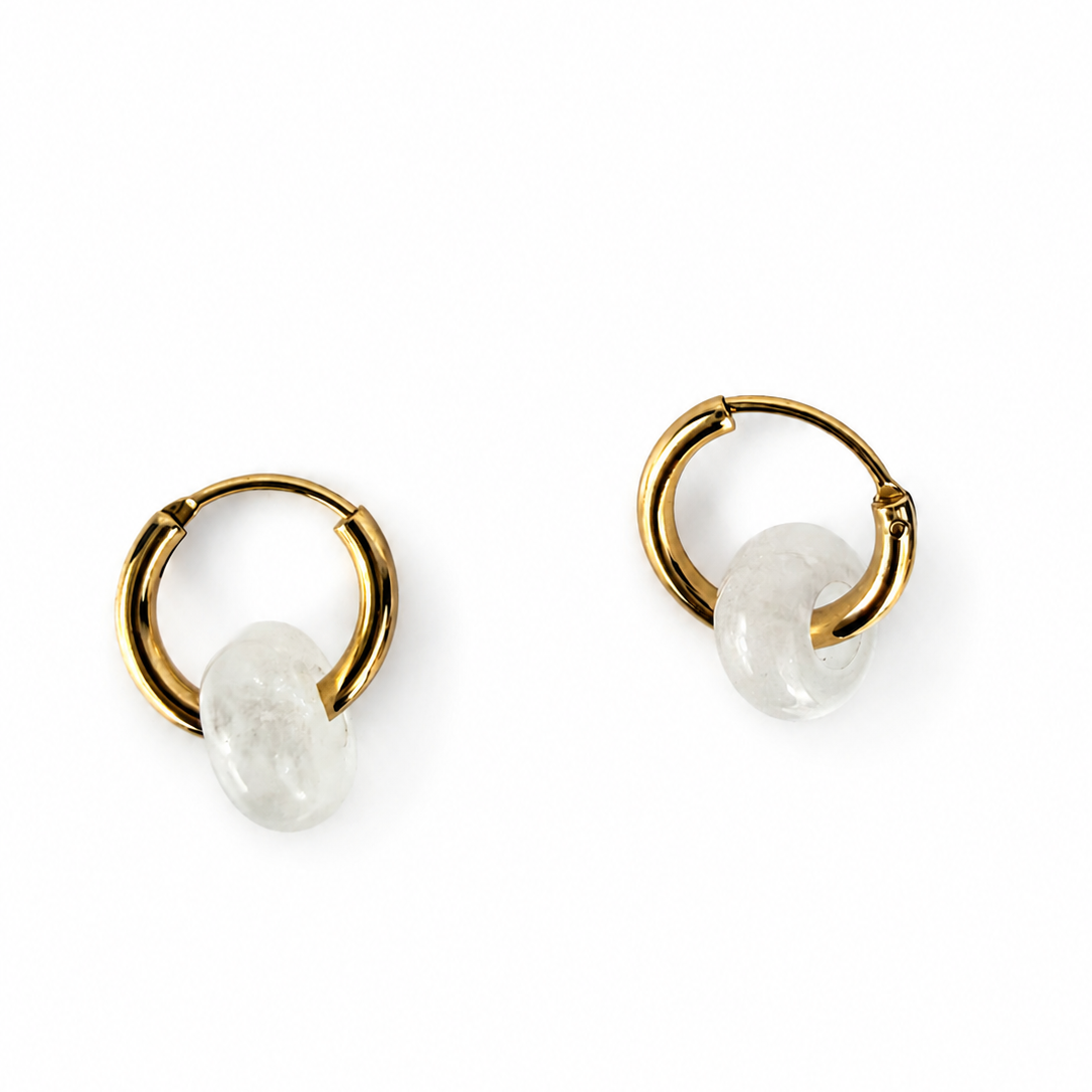 A pair of gold huggie hoop earrings with a small, irregular white stone drop charm, shown on a plain white background.