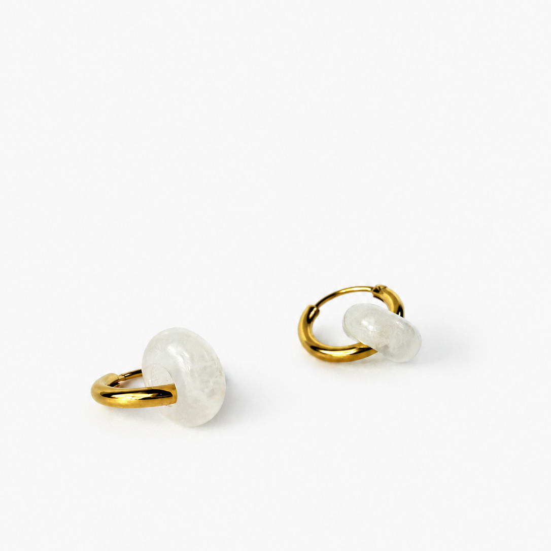 A pair of gold hoop earrings with a small, polished white stone accent, photographed on a clean white background.