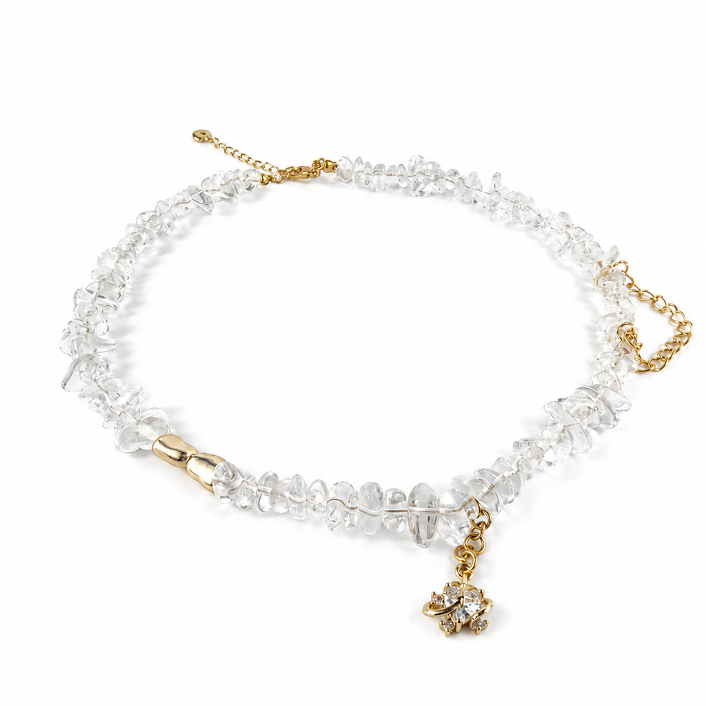 A clear crystal choker necklace with gold-tone chain details and a small gold elephant charm, displayed on a clean white background.