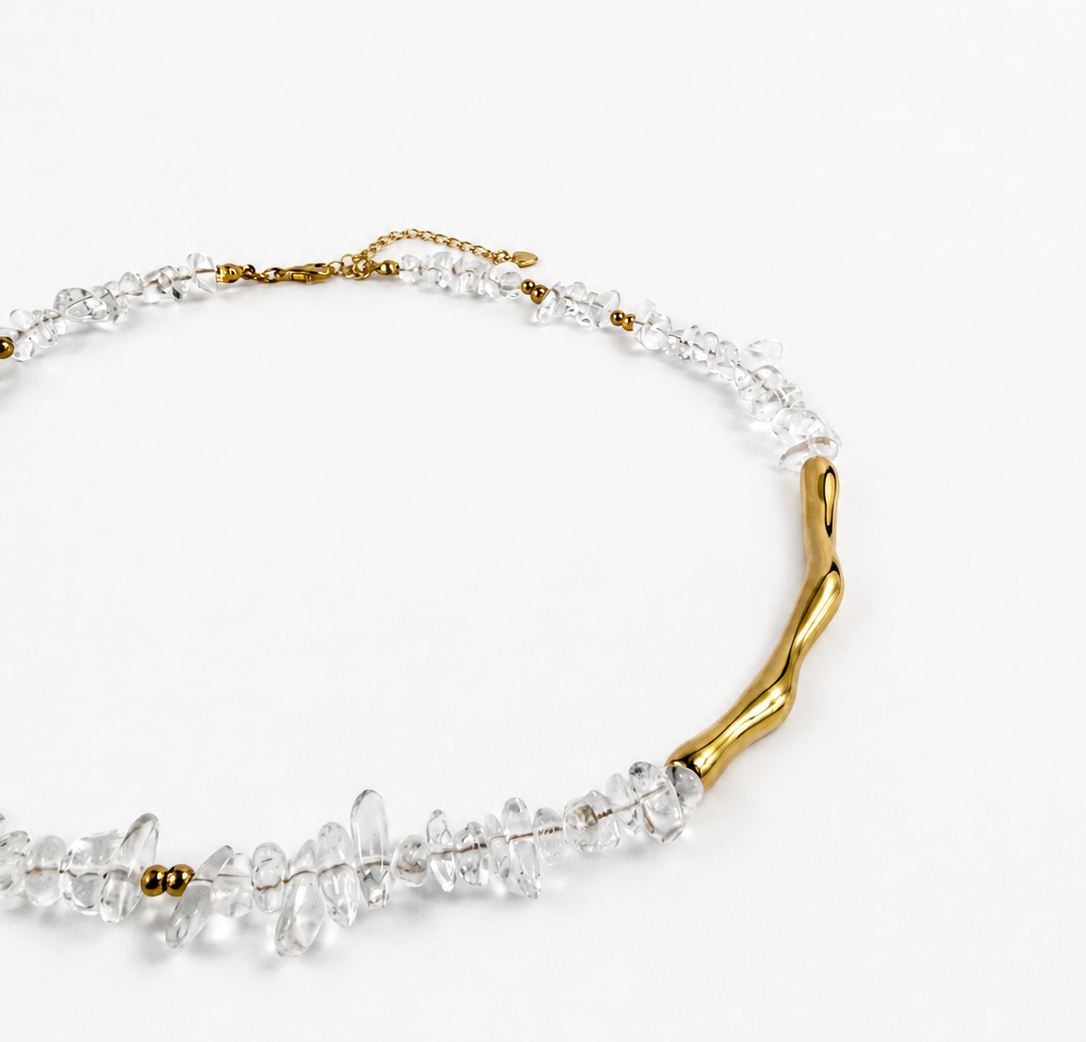 A delicate necklace featuring clear faceted crystal-like beads and a single organic-shaped gold branch element, photographed on a clean white background.