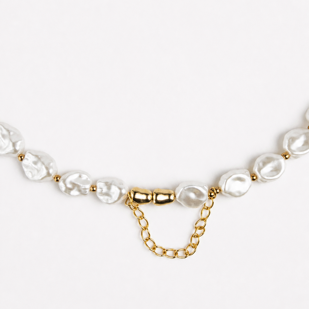 A close-up of a necklace featuring irregular white baroque pearls and a gold chain extender clasp on a clean white background.