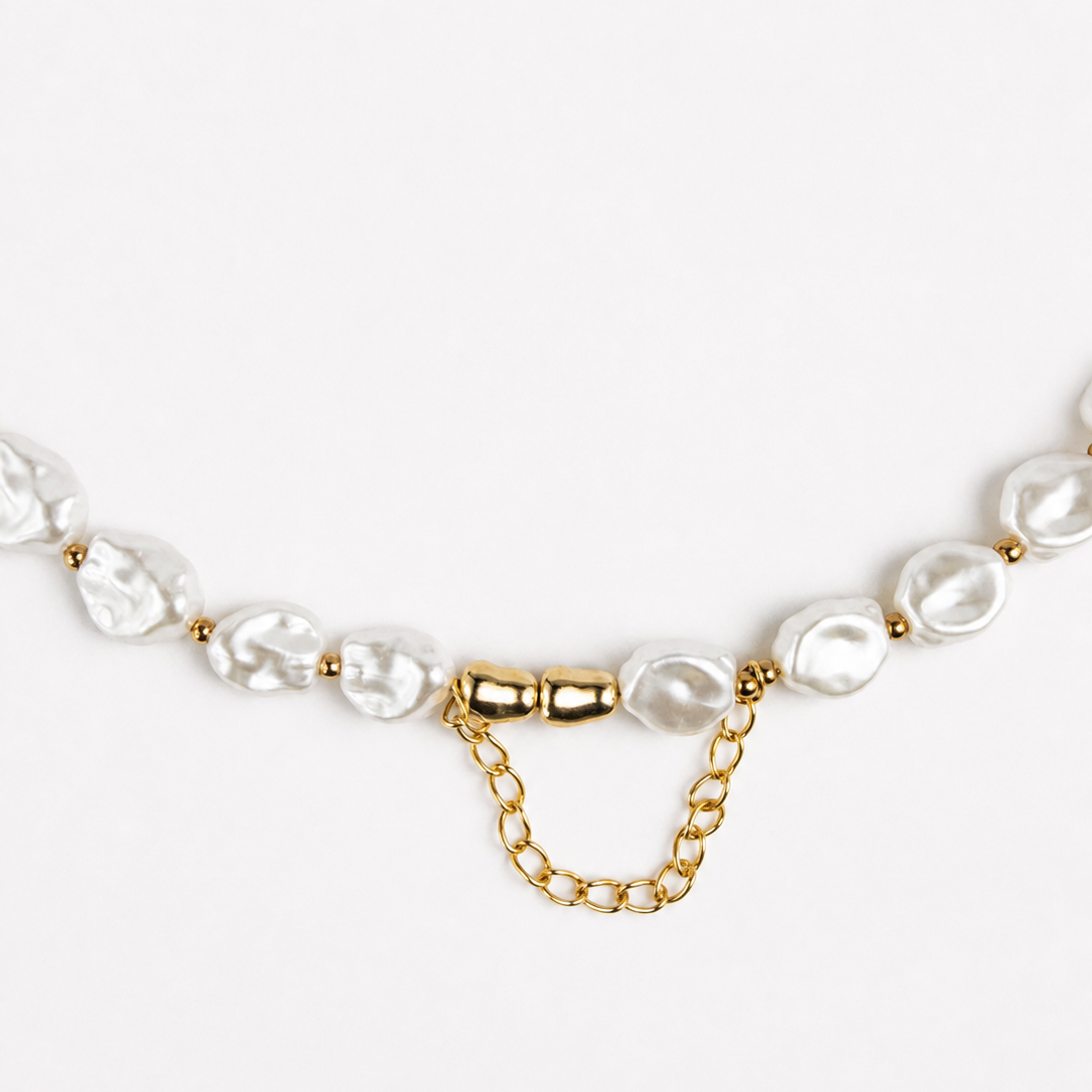 A close-up of a necklace featuring irregular white baroque pearls and a gold chain extender clasp on a clean white background.