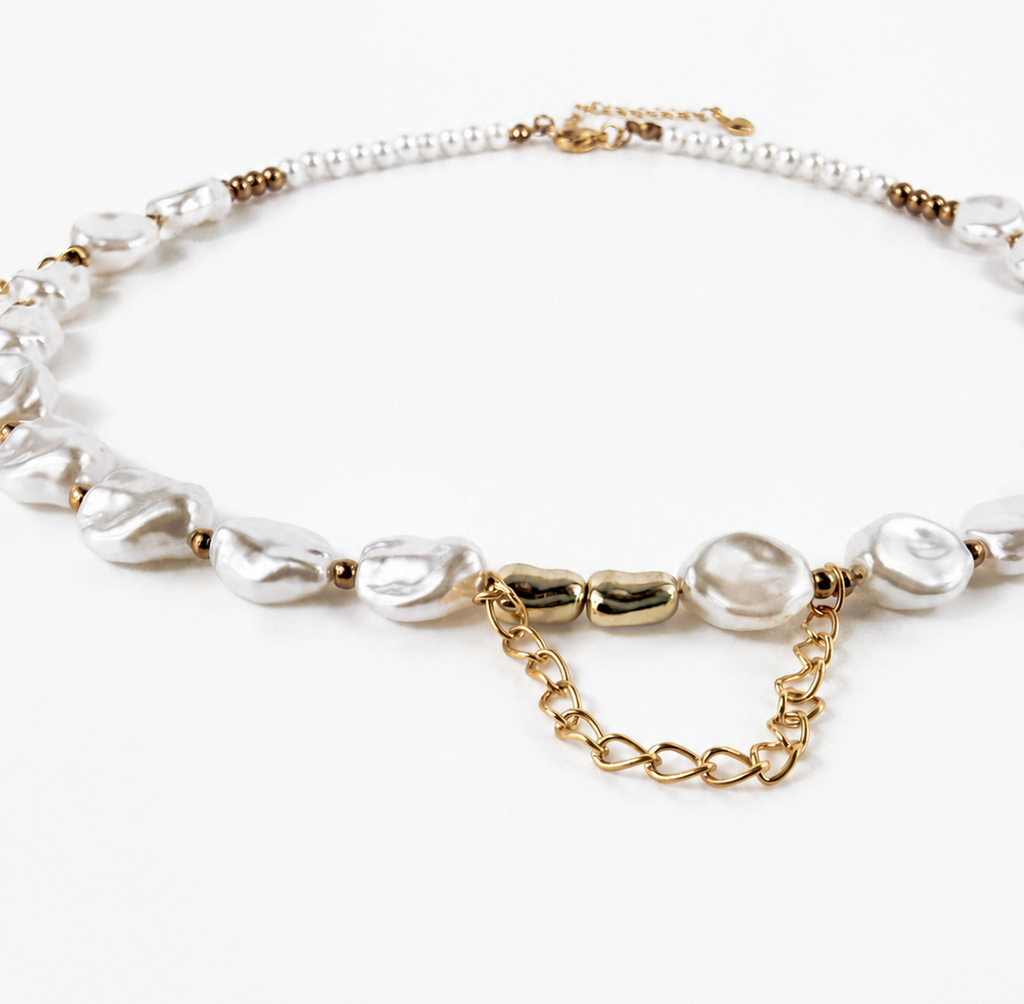 A delicate necklace featuring irregular white baroque pearls, a strand of small white pearls, and gold-tone chain links and clasp details, displayed on a clean white background.
